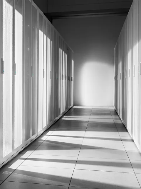 A long, sunlit aisle between rows of white server cabinets with perforated doors
