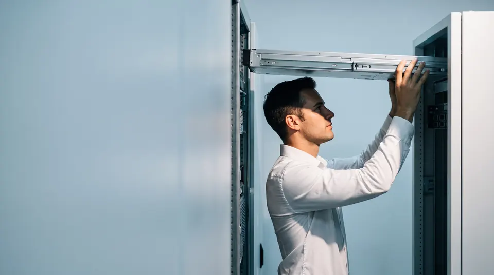 An engineer in a white shirt sliding a server into an open equipment rack